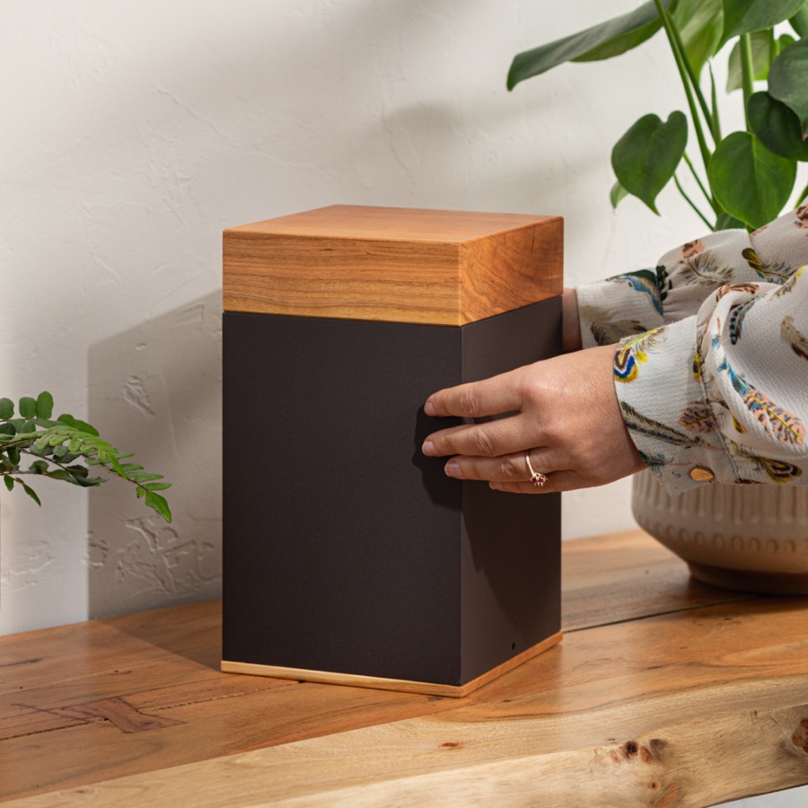 Dark brown urn with a wooden lid on a wooden shelf